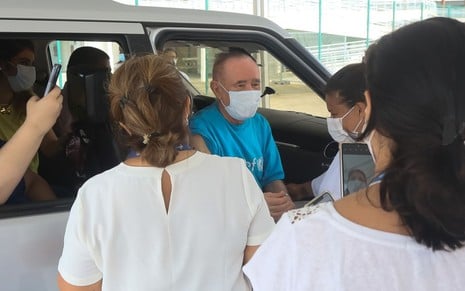 No carro e de máscara, Renato Aragão é vacinado enquanto interage com profissionais de saúde