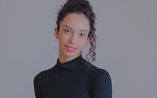 A atriz Agnes Brichta, com uma blusa preta gola alta e o cabelo preso