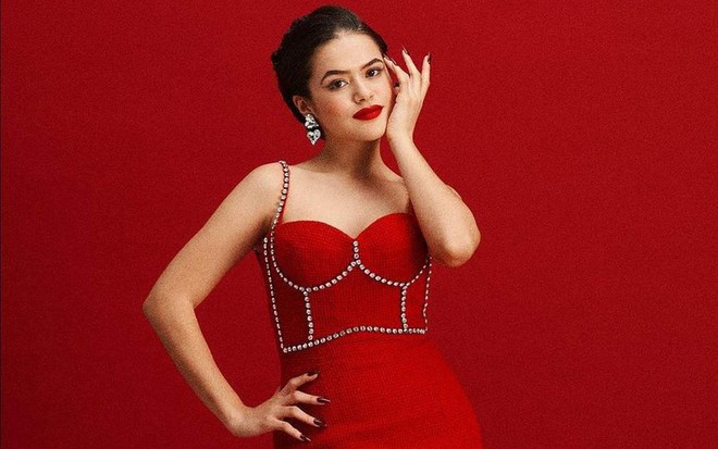 A apresentadora Maisa Silva posa para foto. De vestido vermelho, ela coloca a mão no rosto suavemente