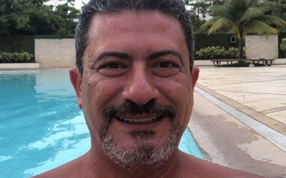 Imagem de Tom Veiga (1973-2020) sorrindo, em frente a uma piscina