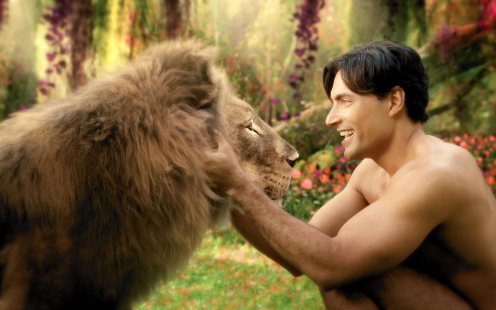 O ator Carlo Porto sorri para um leão, feito com efeitos especiais, em cena como Adão em Gênesis