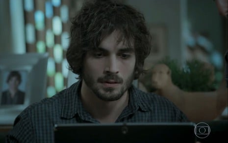 Fiuk (Ruy) olha sério para um tablet em cena de A Força do Querer