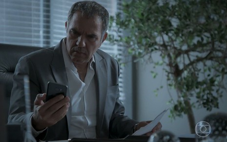 Eurico (Humberto Martins) olha sério para o celular em cena de A Força do Querer