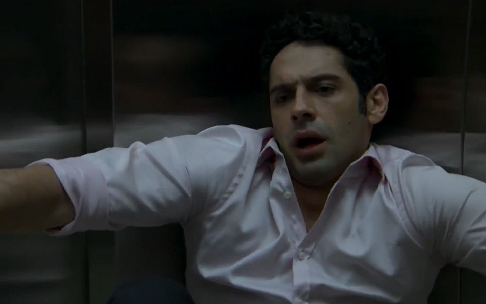 Beto (João Baldasserini) sentado no chão do elevador passando mal em cena de Haja Coração