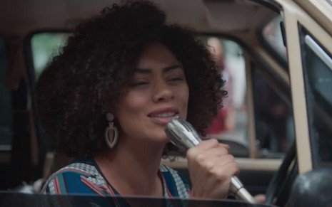 Dóris (Ana Flavia Cavalvanti) dentro de um carro falando no microfone em cena de Malhação