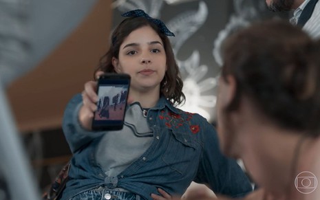 Keyla (Gabriela Medvedovski) mostra a tela do celular para Deco (Pablo Morais) em cena de Malhação