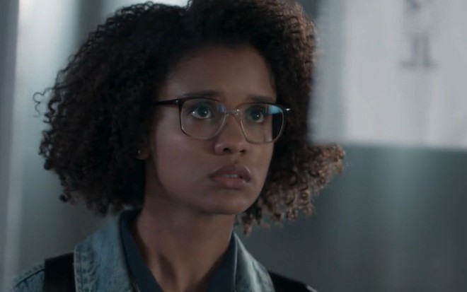 Ellen (Heslaine Vieira) com expressão triste olhando para o espelho em cena de Malhação
