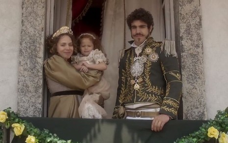 Leopoldina (Leticia Colin) com uma criança no colo na sacada ao lado de dom Pedro (Caio Castro)