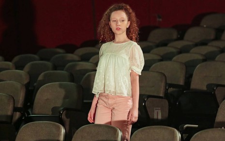 Ester (Manuela Kfouri) em pé na plateia de um teatro em cena de As Aventuras de Poliana