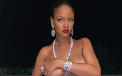 Rihanna posou com olhar distraído, usando o colar polêmico, fazendo topless e escondendo os seios com um dos braços