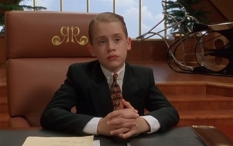 Macaulay Culkin, de terno e gravata, assume a empresa da família em cena de Riquinho (1994)