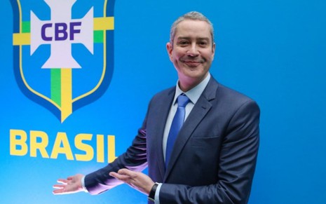 Presidente da CBF, Rogério Caboclo, de terno, em frente ao símbolo da Seleção Brasileira