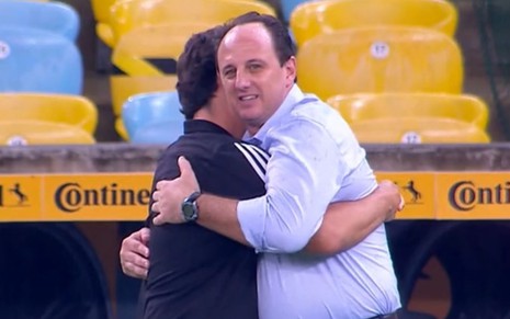 O técnico Rogério Ceni olha para a câmera enquanto abraça Fernando Diniz em jogo no Maracanã