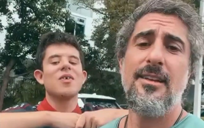 Marcos Mion e seu filho, Romeu, em um lugar a céu aberto, gravando um vídeo em formato de selfie