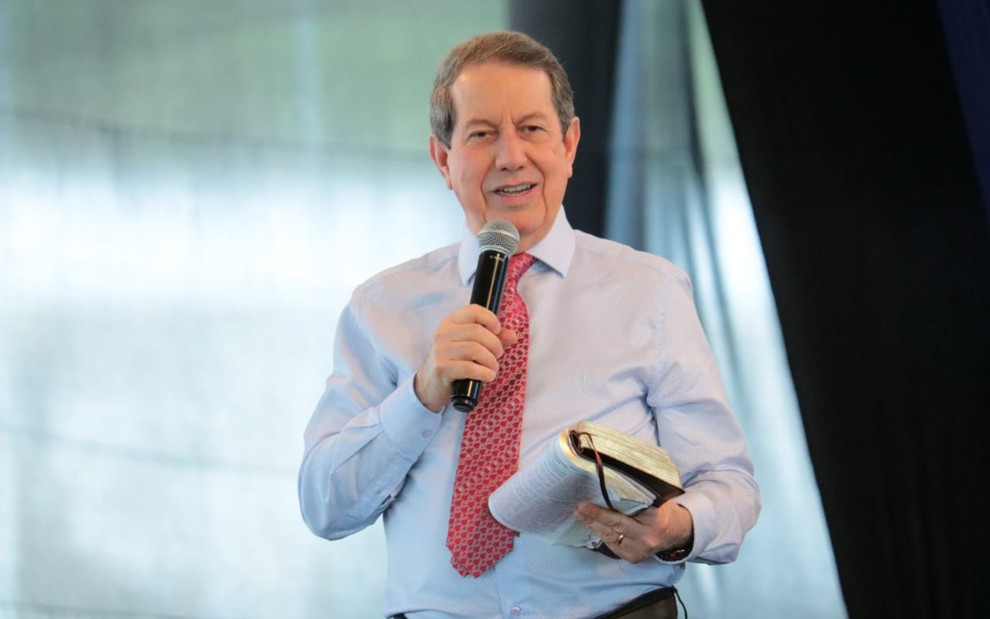 Missionário R.R. Soares com um microfone em uma mão e a bíblia em outra