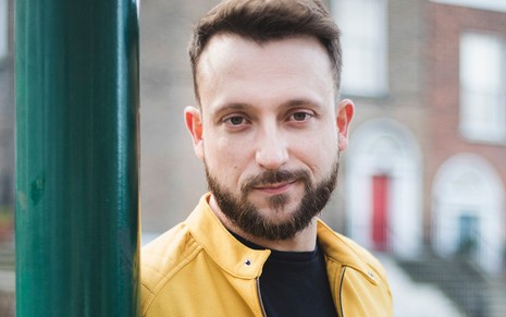 Com jaqueta amarela, Rodrigo Ternevoy posa para foto profissional apoiado em um poste verde