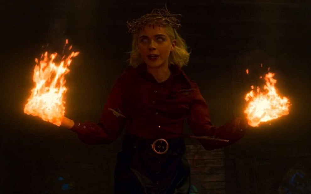 Kiernan Shipka com olhos brancos e fogos nas mãos em cena da série O Mundo Sombrio de Sabrina