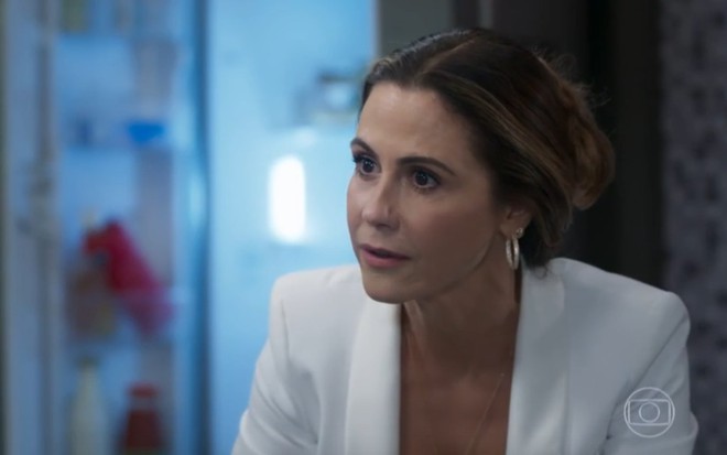 A atriz Guilhermina Guinle com expressão séria, terno branco e coque no cabelo em cena de Salve-se Quem Puder
