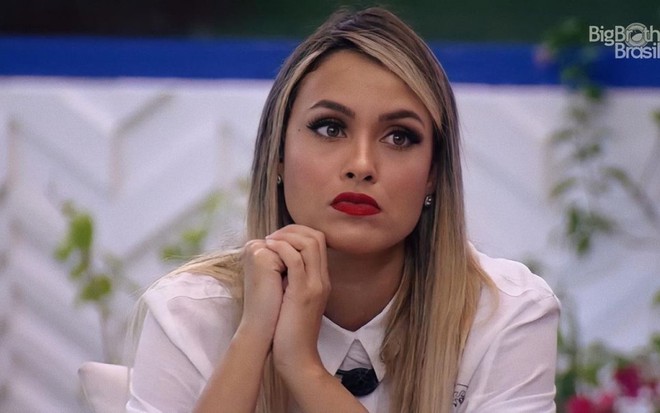 Sarah Andrade com camisa branca, batom vermelho e semblante apreensivo na área externa do BBB21