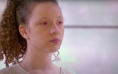 Manuela Kfouri em cena como a personagem Ester, que está com os olhos robóticos vermelhos, em As Aventuras de Poliana