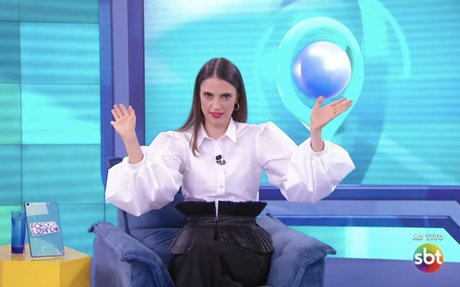 Chris Flores de blusa branca, sentada, apresentando o Fofocalizando