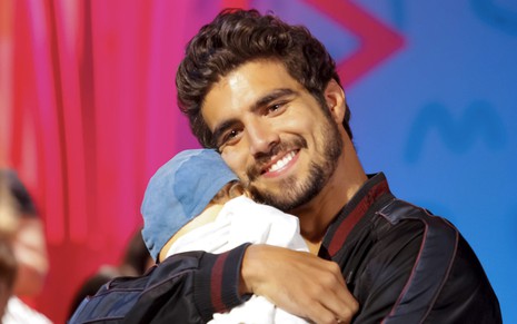 O ator Caio Castro abraçado a um boneco durante participação no programa da Maísa