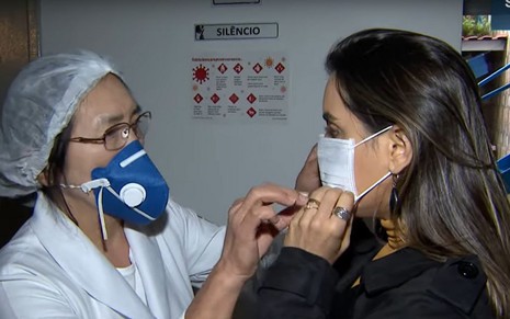 Reportagem do SBT em que mostra uma mulher ajudando uma repórter a colocar uma máscara no rosto