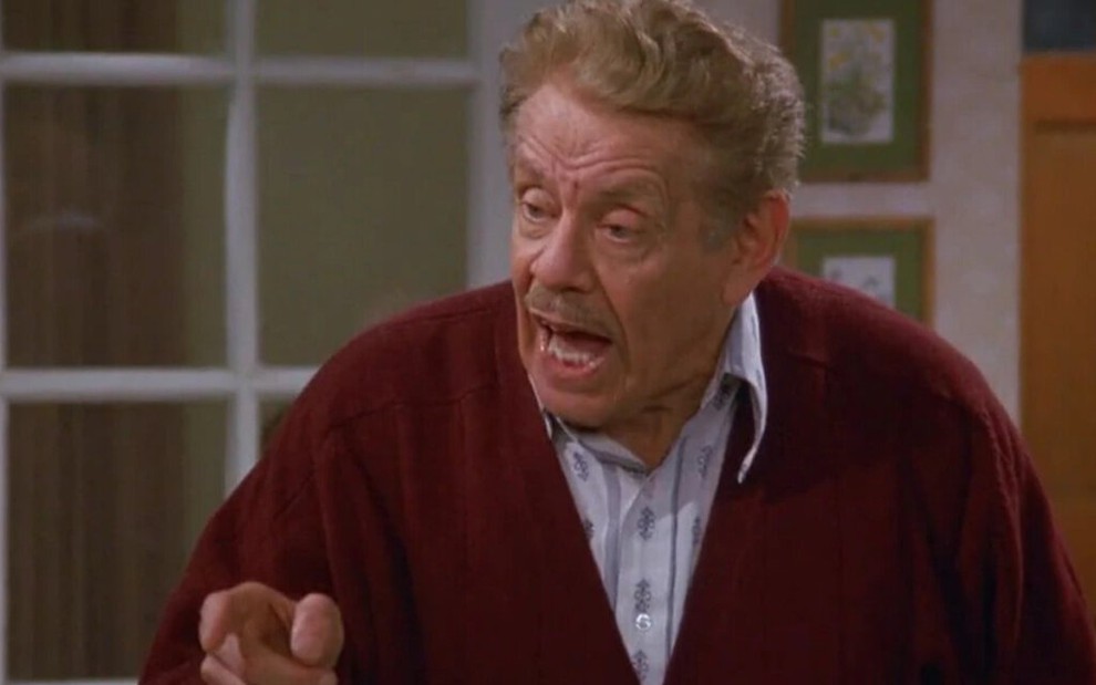 Com uma bulsa de frio em cima de uma camisa social, Jerry Stiller aponta o dedo e grita em cena de Seinfeld