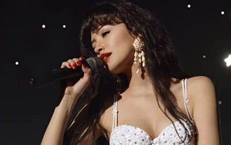 Christian Serratos canta com um microfone em cena de Selena: A Série