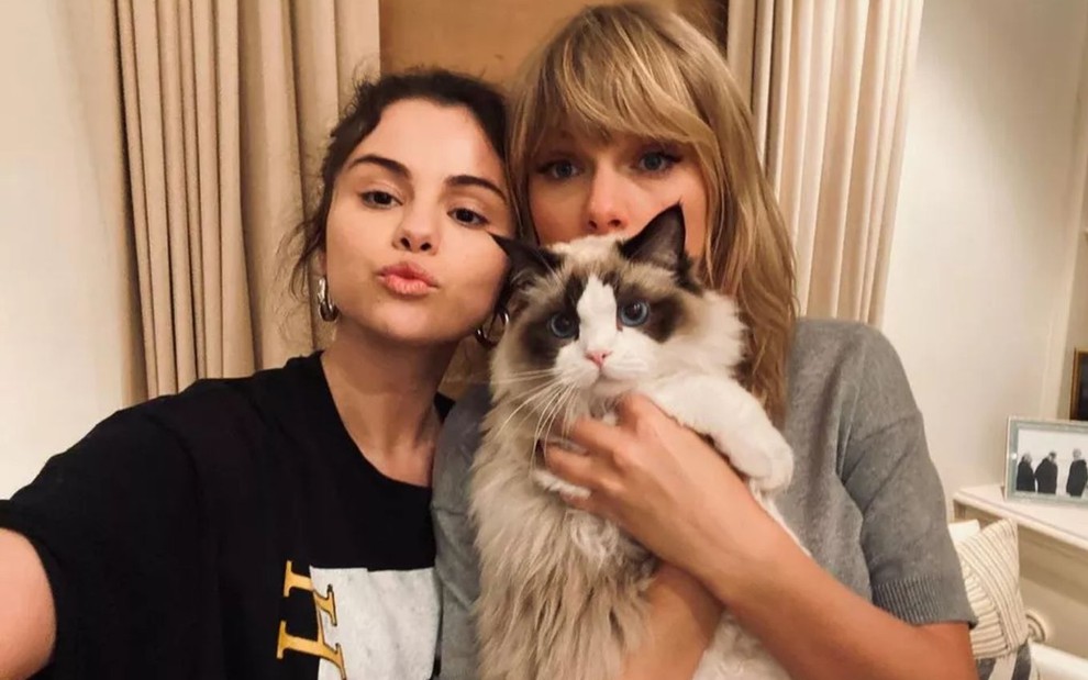 Imagem de Selena Gomez (à esq.) e Taylor Swift segurando um gato