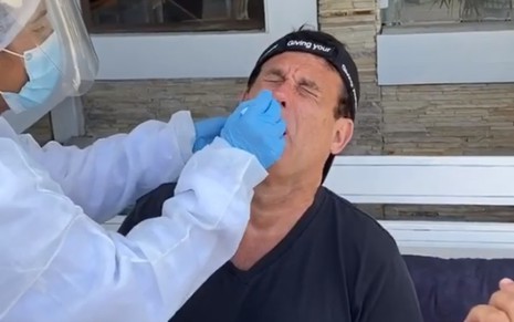 Sérgio Mallandro faz careta enquanto um profissional com luvas aplica um cotonete em seu nariz