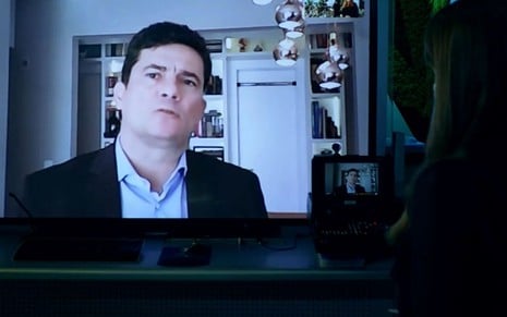 Sergio Moro em um telão conversa virtualmente com Poliana Abritta, que está de costas na imagem
