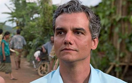 Wagner Moura caracterizado como personagem do filme Sergio, da Netflix, de camisa azul, próximo a floresta