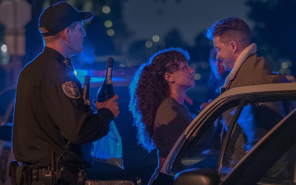 Ashley (Jasmine Cephas Jones) e Miles (Rafael Casal) no lado direito olhando um para o outro sendo observados por um policial no lado esquerdo