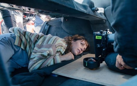 Bárbara (Maggie Civantos) deitada em um porta-mala falso de um carro olhando para a câmera no lado direito