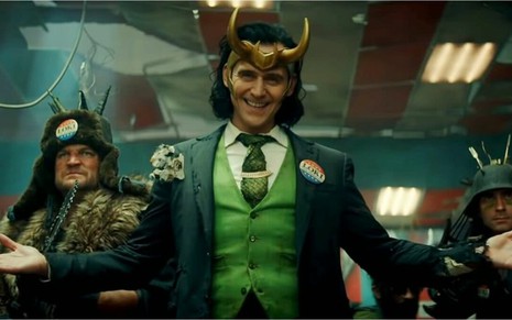 Loki (Tom Hiddleston) ao centro da foto de paletó e capacete com chifres em cena da série