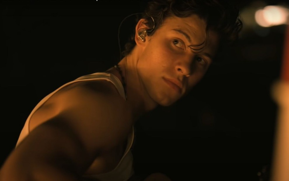 O cantor Shawn Mendes está meio de perfil em um ambiente com pouca iluminação em cena do documentário Shawn Mendes: In Wonder