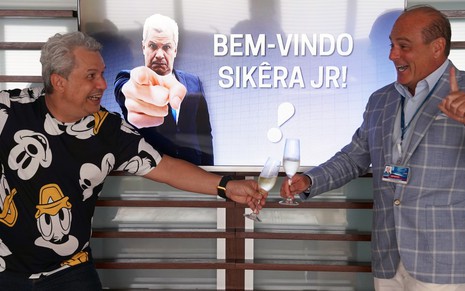 Sikêra Jr. veste camiseta com estampas do Mickey e segura taça com espumante para brindar com Marcelo de Carvalho na RedeTV!