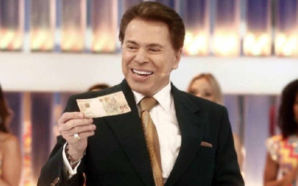 Silvio Santos sorri e mostra uma nota de R$ 50 no palco de seu programa no SBT