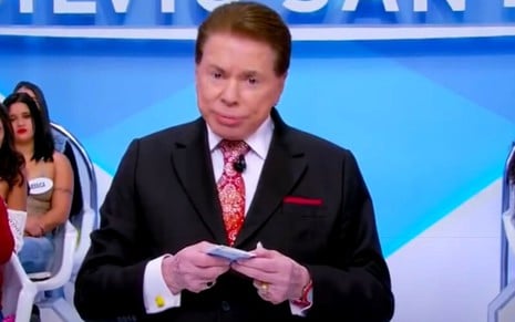 Com expressão de dúvida, Silvio Santos olha para a câmera no cenário de seu programa no SBT