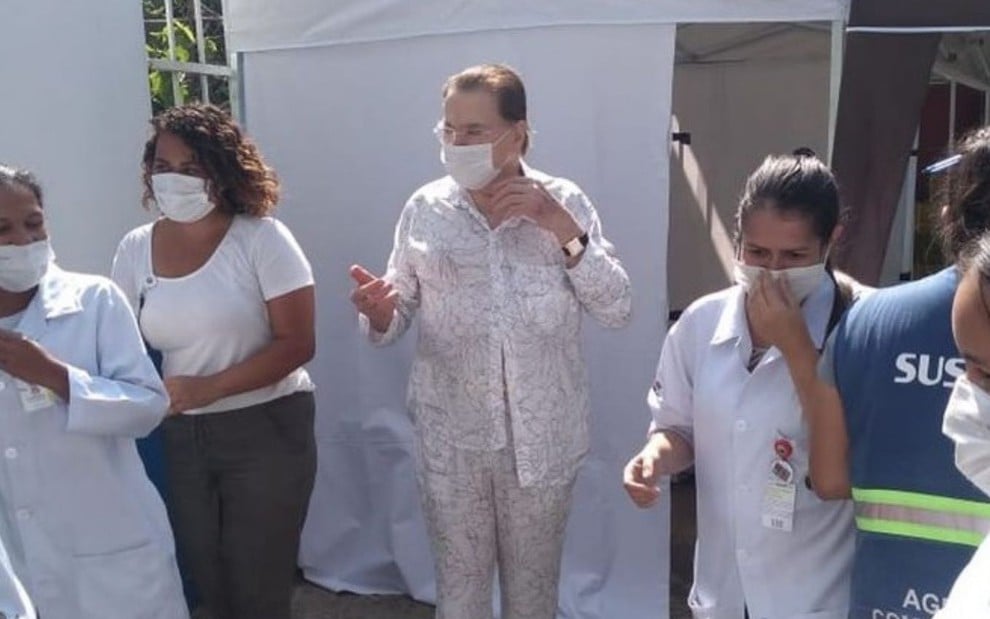 Silvio Santos todo de branco e de máscara após ser vacinado em São Paulo, com profissionais da saúde