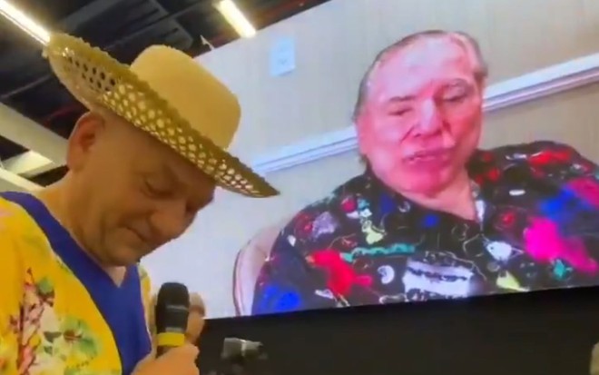 Silvio Santos sem peruca, de cabelo branco, em telão na festa de aniversário de Luciano Hang, o "véio da Havan"