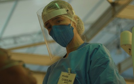 Imagem de Marjorie Estiano vestida de médica, com máscara e face shield em cena de Sob Pressão: Plantão Covid