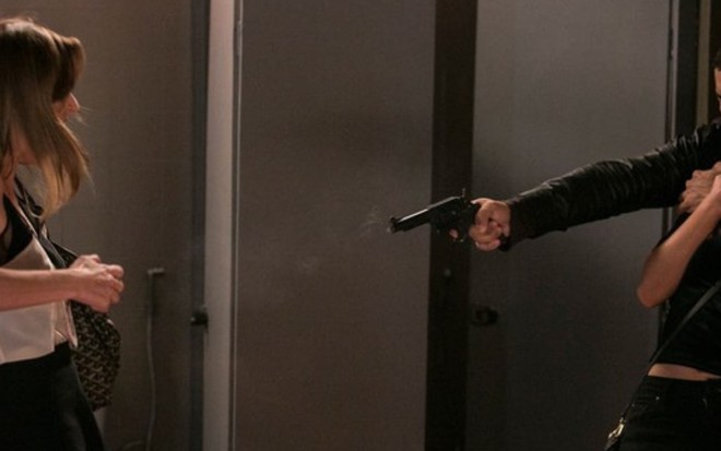 Sofia (Priscila Steinman) aparece levando um tiro de Jacaré (Sergio Malheiros), que aponta a arma para comparsa e segura Eliza (Marina Ruy Barbosa) em Totalmente Demais