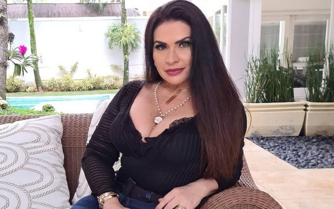 Imagem de Solange Gomes sentada em um sofá, com blusa preta e cabelo solto