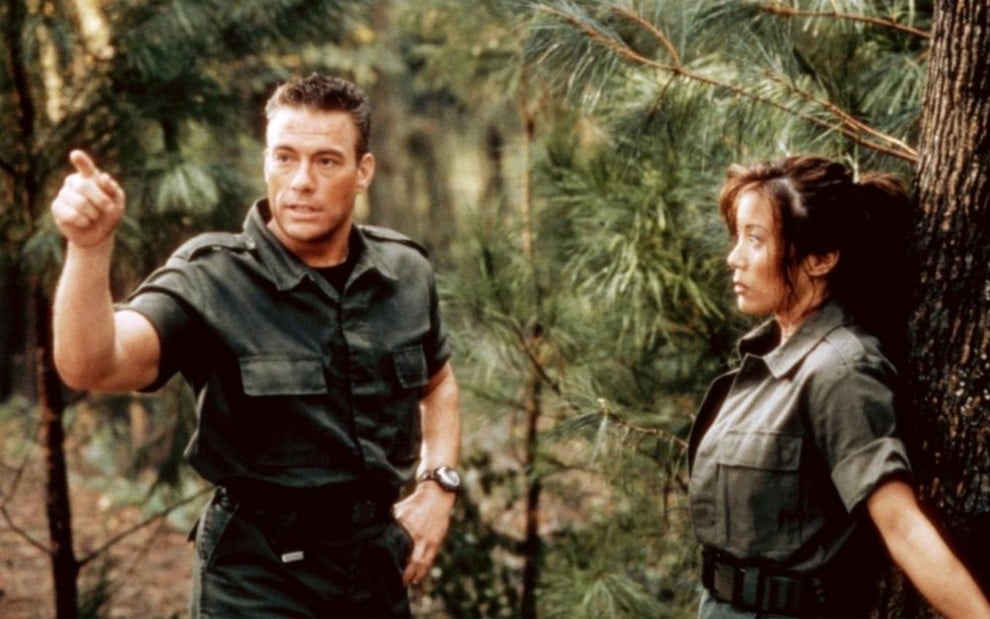 Em um fundo de mata verde, Jean-Claude Van Damme e Kiana Tom contracenam em Soldado Universal - O Retorno (1999)