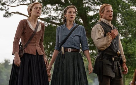 Brianna (Sophie Skelton), Claire (Caitriona Balfe) e Jamie (Sam Heughan) aparecem com expressões de choque em cena da quinta temporada de Outlander