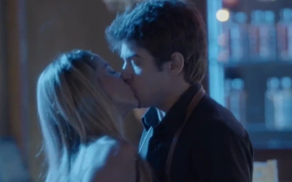 No ambiente da boate com luz azul, Suely (Danielle Winits) beija Charles (Raphael Sander) em cena de Totalmente Demais