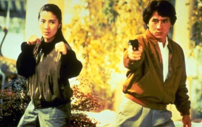 Michelle Yeoh com os braços posicionados para lutar; ao seu lado está Jackie Chan com uma arma apontada para a frente