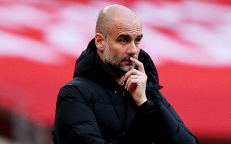 O técnico Pep Guardiola pensativo enquanto comanda o Manchester City